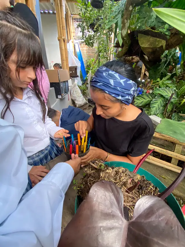 Niños y niñas siembran semillas identificadas con palitos de colores en una maceta