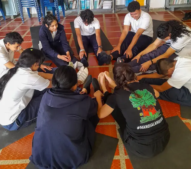 Estudiantes se apoyan mutuamente en un ejercicio de estiramiento en círculo